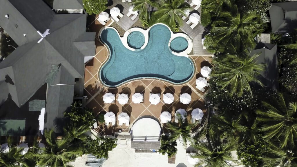 Aerial view on luxury house at the beach with palm trees and swimming pool. Top view aerial shot of the seascape with white sand and turquoise water and lonely pier
