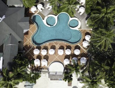 Aerial view on luxury house at the beach with palm trees and swimming pool. Top view aerial shot of the seascape with white sand and turquoise water and lonely pier